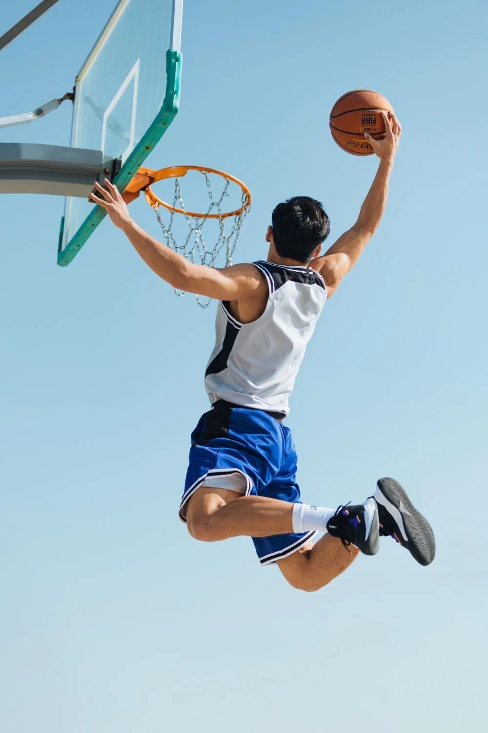 Basketball player leaping towards the hoop against a clear sky